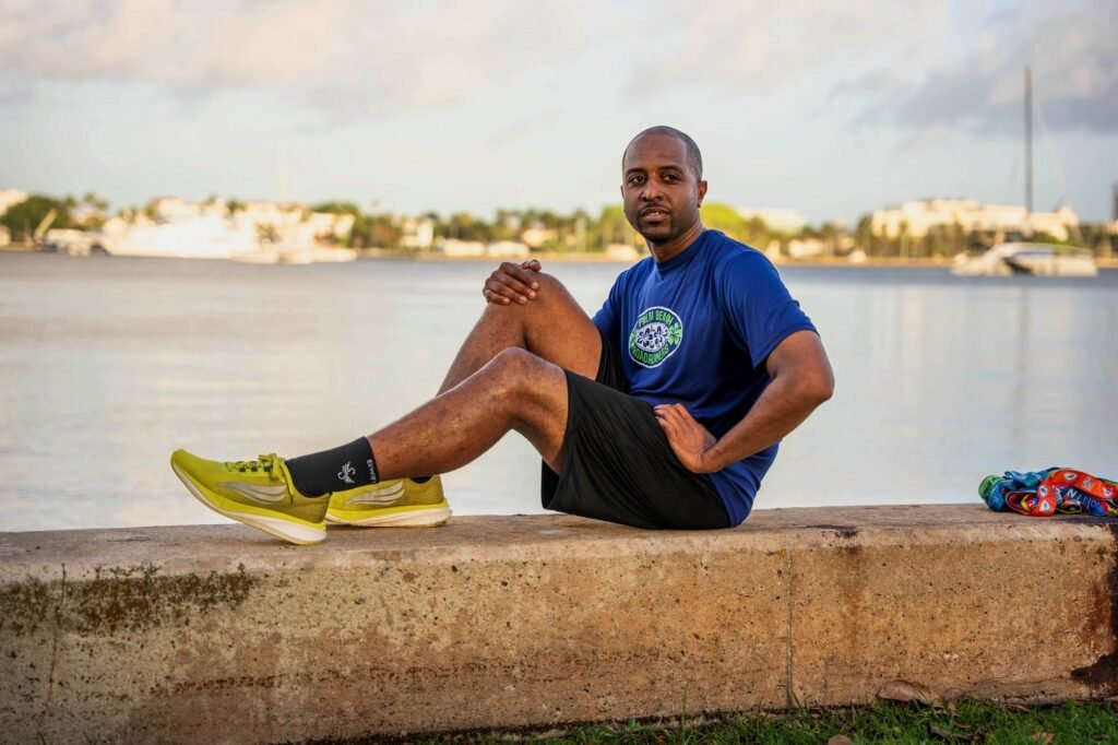 Runner in a blue club shirt and yellow running shoes sitting on a seawall by the Intracoastal in West Palm Beach