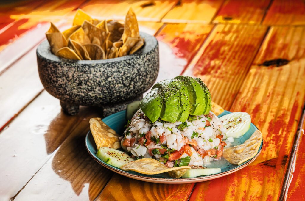 Shrimp ceviche topped with avocado next to a molcajete of tortilla chips, restaurant food photography