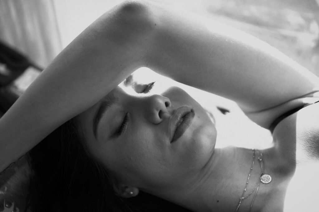 Intimate black and white boudoir portrait of a woman with her arm over her head and eyes closed in window light — boudoir photography in Palm Beach and Miami by Felipe Restrepo