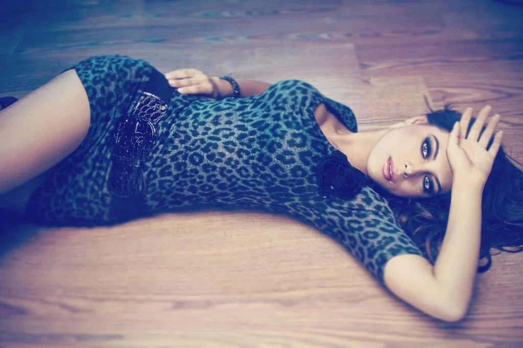 Woman in a leopard print dress lying on a wooden floor in soft blue light, editorial boudoir portrait