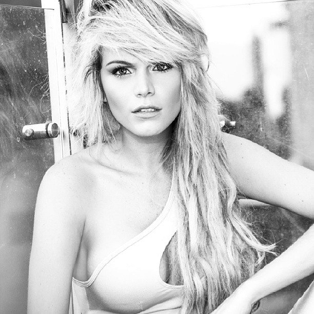 Black and white beauty portrait of a blonde woman with tousled hair and a one-shoulder top
