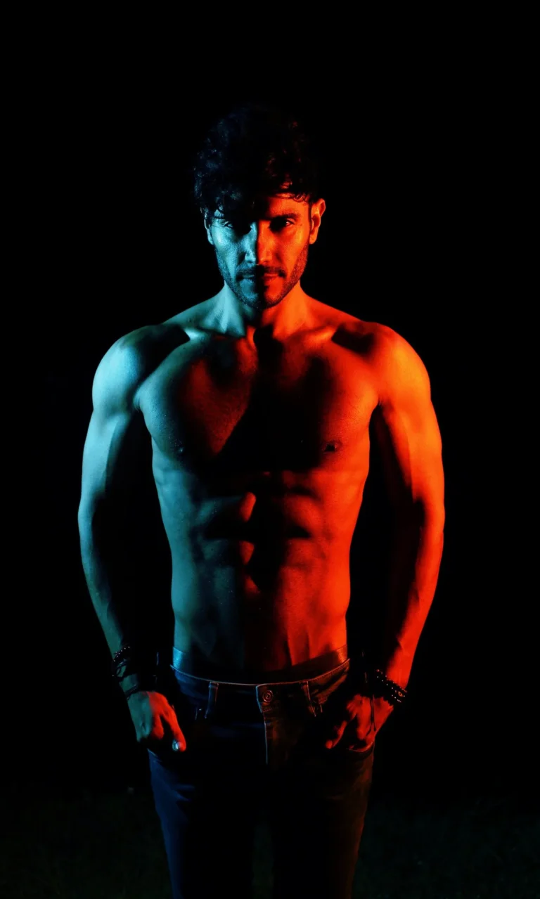 Male model photographed with red and blue gel lighting on a black background, men's fashion and fitness portrait