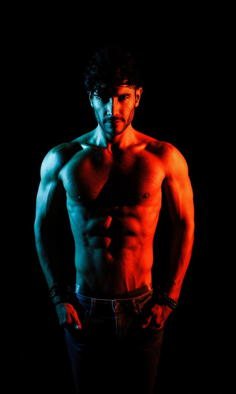 Male model photographed with red and blue gel lighting on a black background, men's fashion and fitness portrait