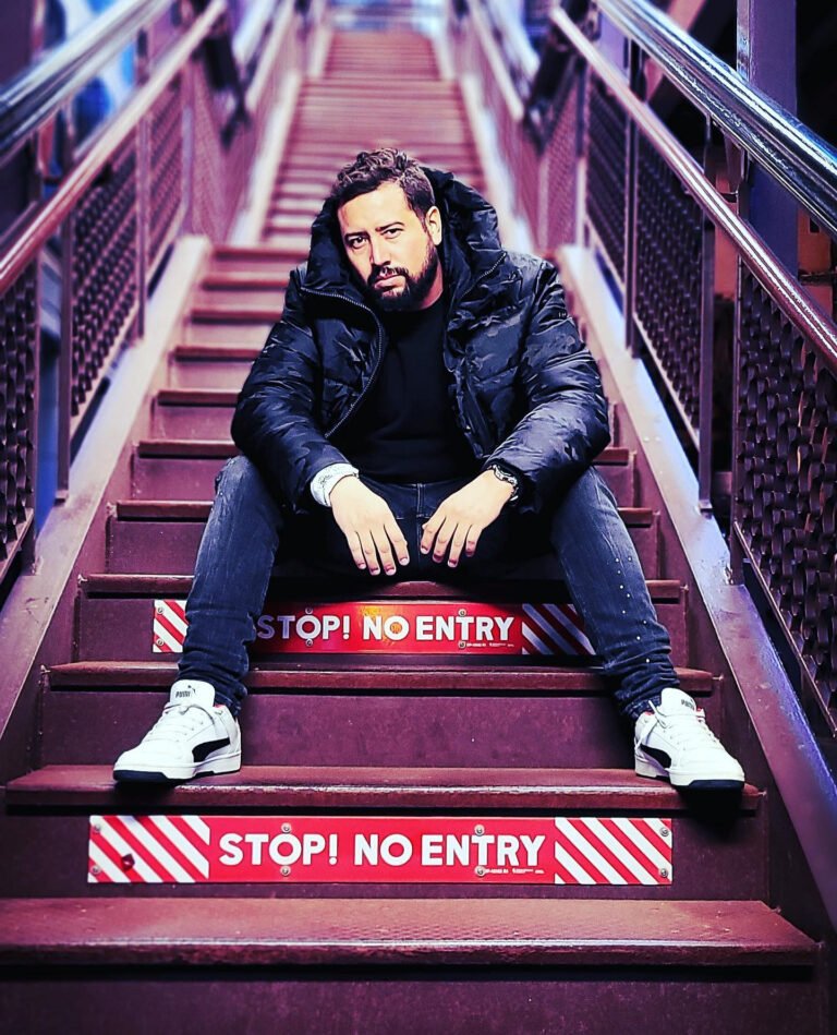 Man in a puffer jacket seated on red and white striped stairs, men's streetwear editorial photography