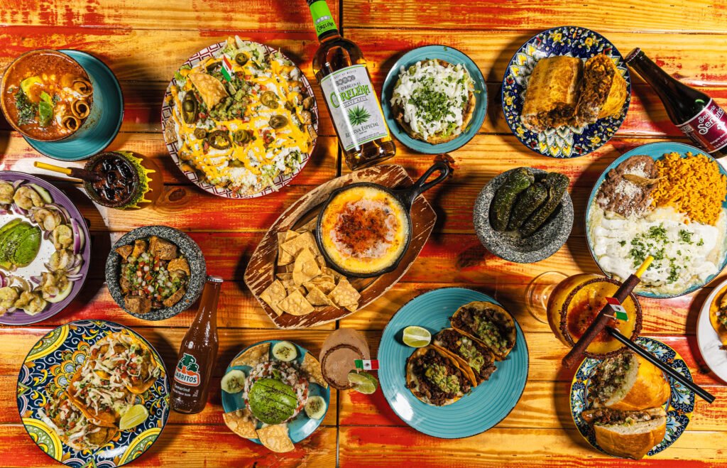 Overhead table spread of Mexican dishes, tacos, nachos and drinks on a colorful wooden table for a restaurant menu