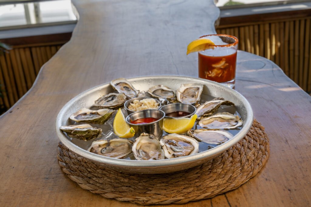 Fresh oysters on ice with lemon, cocktail sauce and mignonette on a metal tray, raw bar food photography