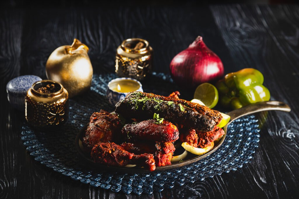 Tandoori mixed grill with seekh kebab in a cast iron skillet, with red onion, lime and green pepper on a dark wood table